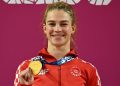 An athlete from Croatia smiles while holding a gold medal, wearing a red jacket with the Olympic Team Croatia logo.